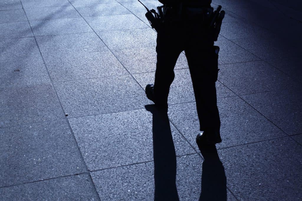 A police officer walking on a dark pavement with a shadow of his legs